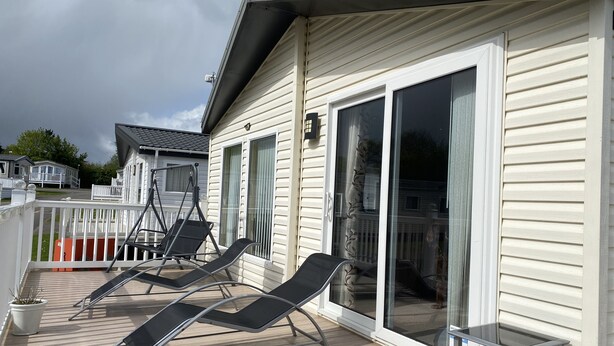 A deck with two lounge chairs, a small table, and a potted plant. - Luxury Air Conditioned holiday Lodge . sleeps 5  Burgh Castle  Great Yarmouth (Burgh Castle)