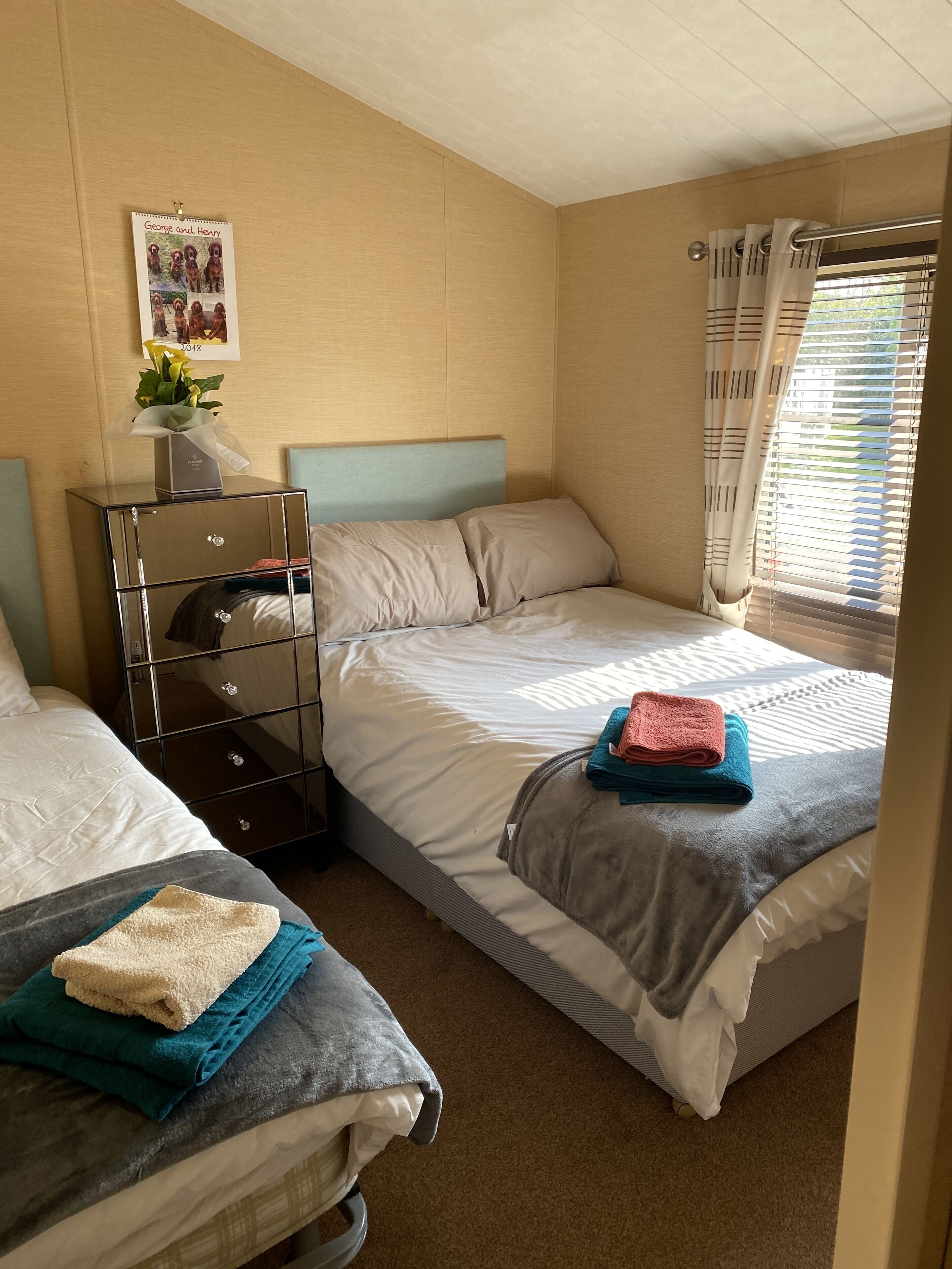 A bedroom with two single beds, a dresser, a mirror, and a window with curtains.