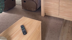 A compact living space with a sofa, a TV mounted on the wall, a small kitchen area, and a ceiling fan. - Luxury Air Conditioned holiday Lodge . sleeps 5  Burgh Castle  Great Yarmouth (Burgh Castle)