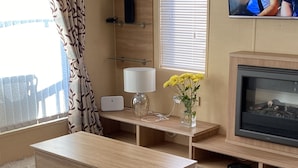 A living room with a wooden coffee table, a sofa, a TV, and a fireplace. - Luxury Air Conditioned holiday Lodge . sleeps 5  Burgh Castle  Great Yarmouth (Burgh Castle)