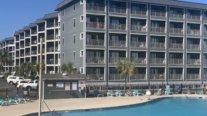 A multi-story hotel with a swimming pool, outdoor seating, and a fenced area. - Beachfront 2-bedroom condo just steps away from sand, surf and sun. (Myrtle Beach)