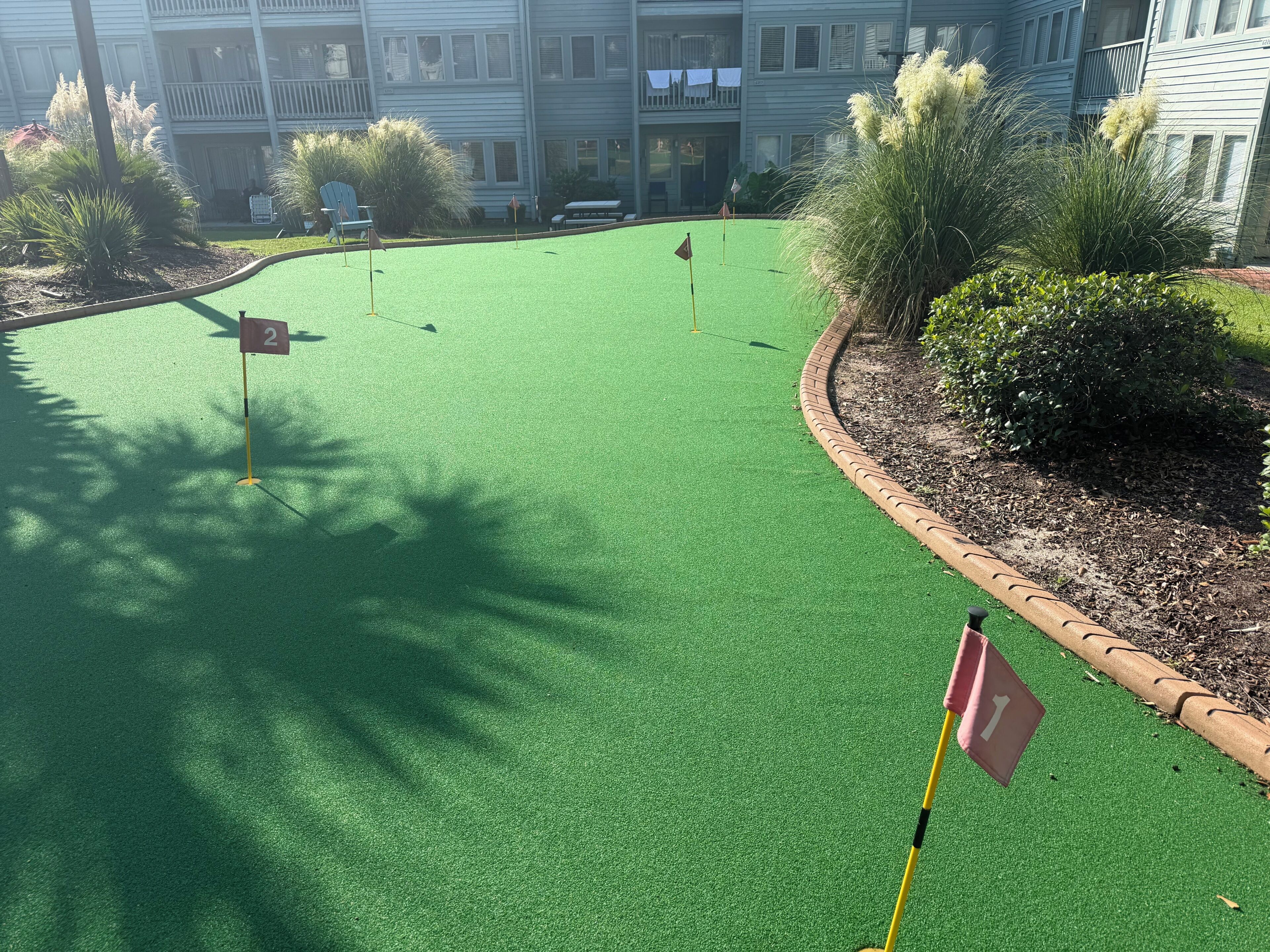 Un campo da minigolf con erba sintetica, buche numerate e aiuole circostanti.
