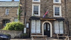 A stone building with a sign reading "The Bake-Well" and a British flag.