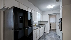 Ett modernt kök med vita skåp, ett svart kylskåp och ett klinkergolv.