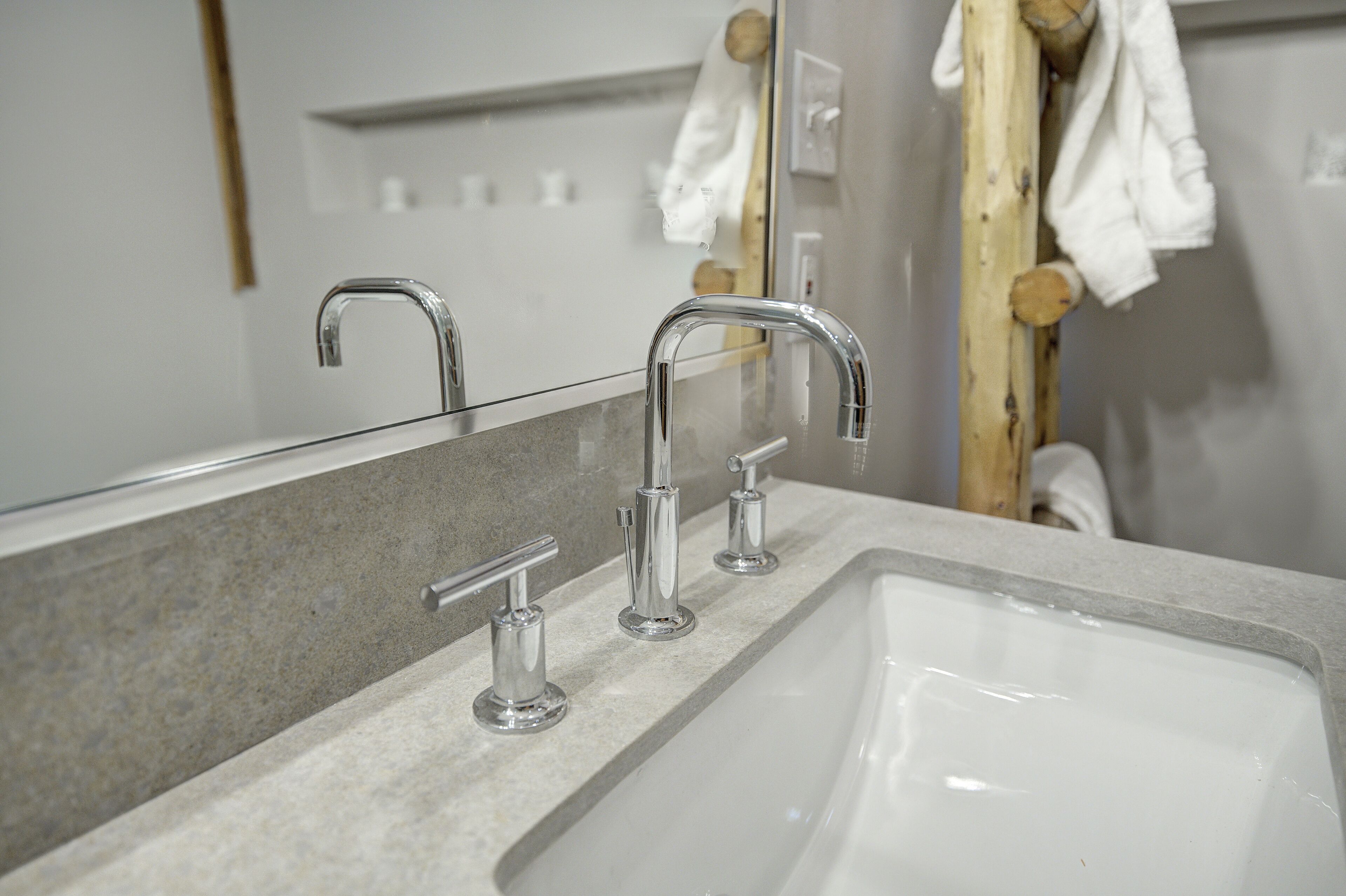 Un baño con un lavamanos blanco, dos grifos cromados y un toallero de madera.