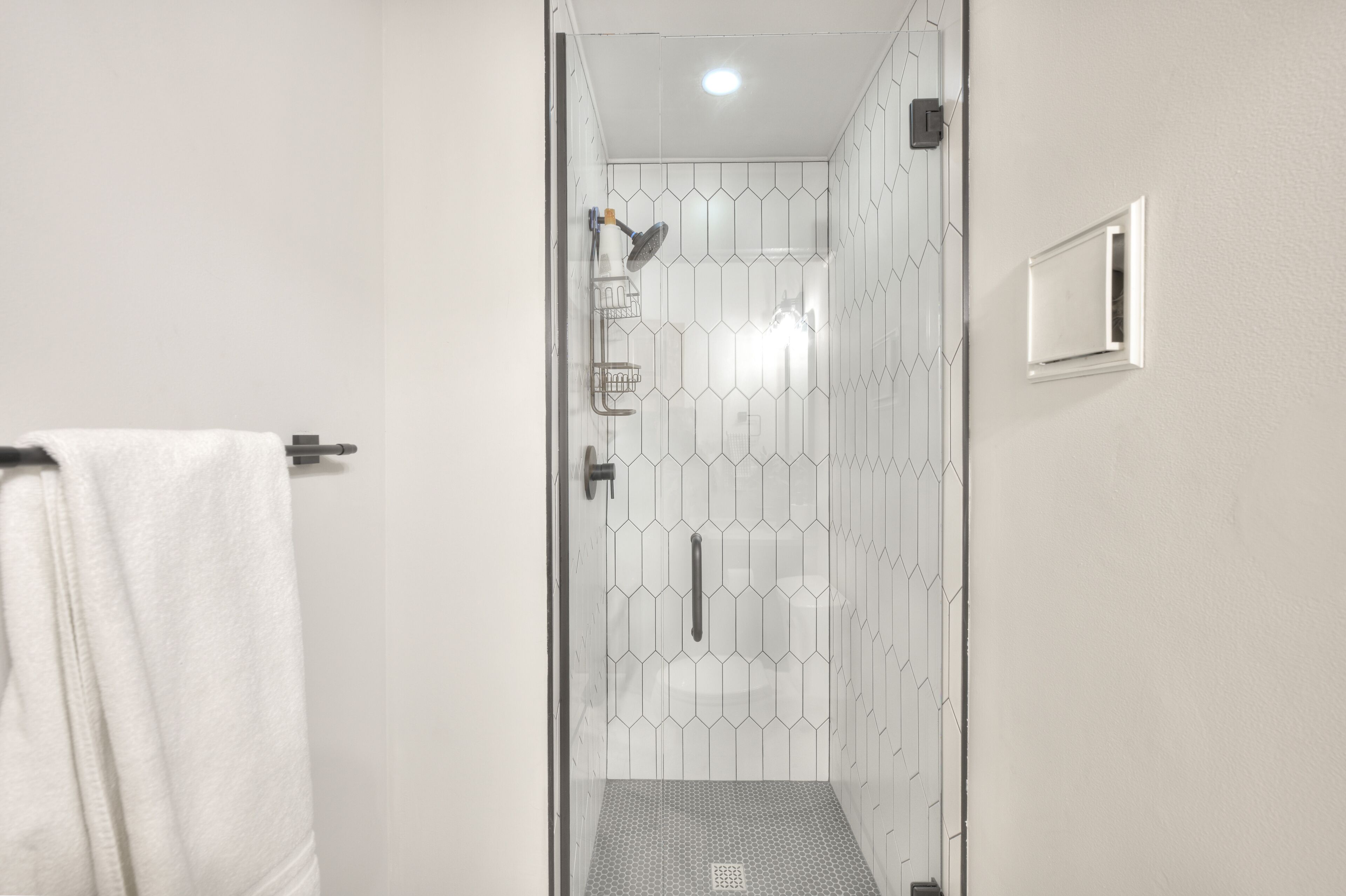 A modern bathroom with a glass shower enclosure, a white towel hanging on the wall, and a small window.