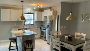 A modern kitchen with white cabinets, a central island, stainless steel appliances, and a dining area with white chairs.