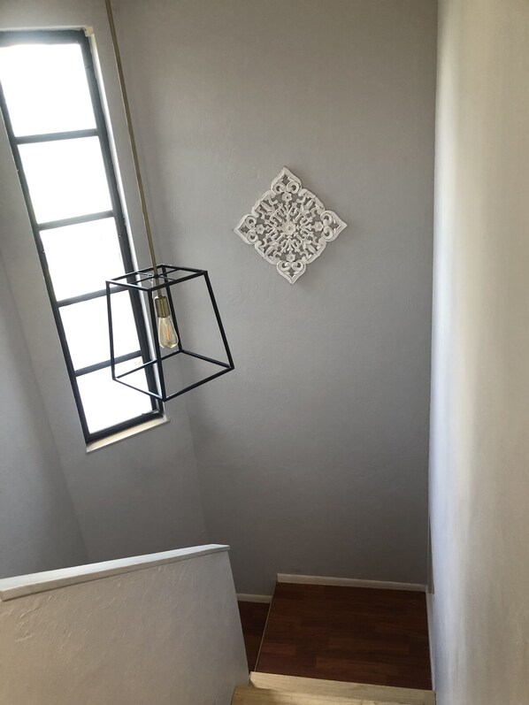 A stairwell with a modern light fixture, a decorative wall piece, and a window allowing natural light.