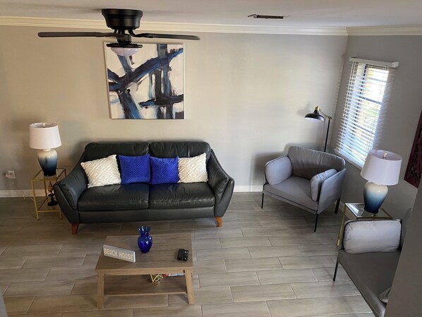 A living room with a black leather sofa, a grey armchair, a wooden coffee table, and a blue vase.