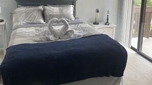 A bedroom with a bed, a ceiling fan, a decorative wall piece, a nightstand, and a view through a window.