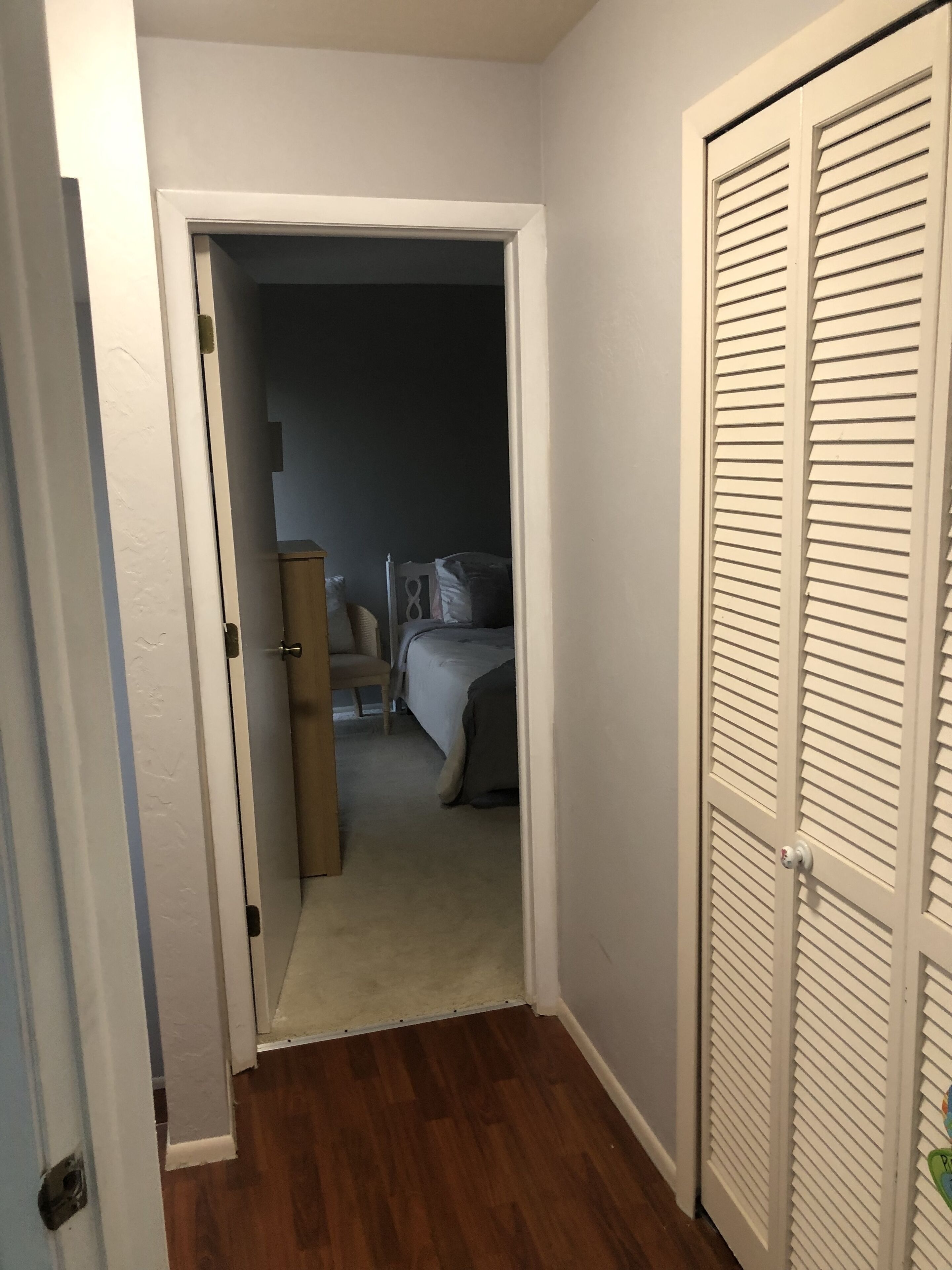 A hallway leading to a bedroom with a bed, a nightstand, and a dresser.