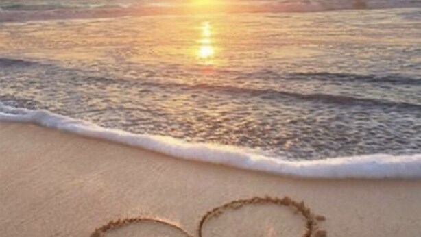A beach scene with a sunset over the ocean, waves gently lapping at the shore, and footprints in the sand.