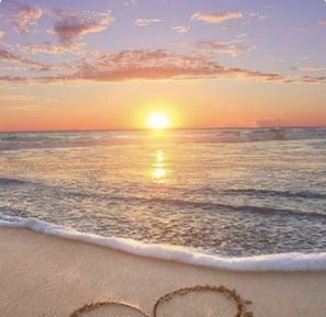 A beach scene with a sunset over the ocean, waves gently lapping at the shore, and footprints in the sand.