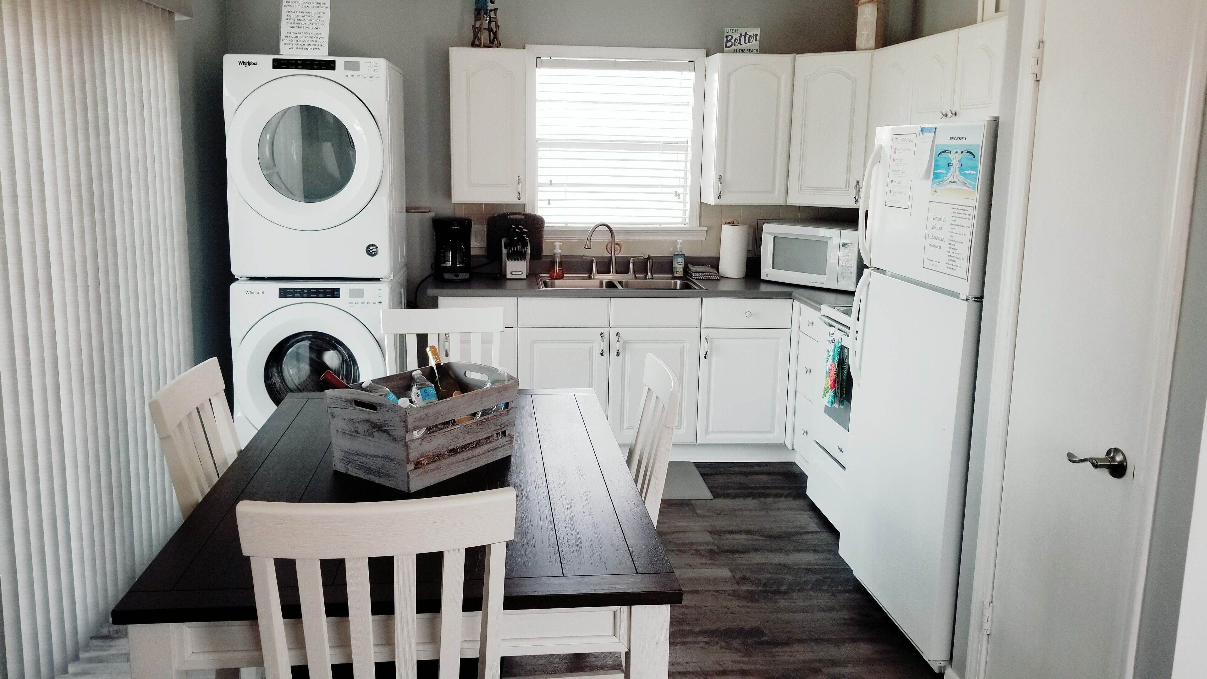 A compact kitchen with a washing machine, a microwave, a refrigerator, and a dining area with a table and chairs.