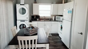 A compact kitchen with a washing machine, a microwave, a refrigerator, and a dining area with a table and chairs. - Blessed A-Shore-ance one short block to the beach with private back deck.  (Panama City Beach)