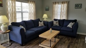 A living room with two dark blue sofas, a wooden coffee table, and a lamp on a side table. - Blessed A-Shore-ance one short block to the beach with private back deck.  (Panama City Beach)