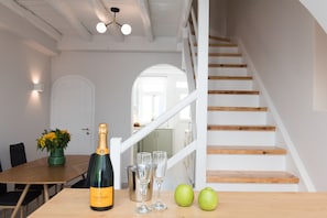 A dining area with a wooden table, a bottle of champagne, two glasses, and two apples.