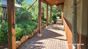 A covered outdoor walkway with wooden beams and a brick path, surrounded by greenery and a wooden fence. - Newly remodeled Old town/2 King Suites
Pet Friendly
Deck/Grill
EV/Carport (Steamboat Springs)