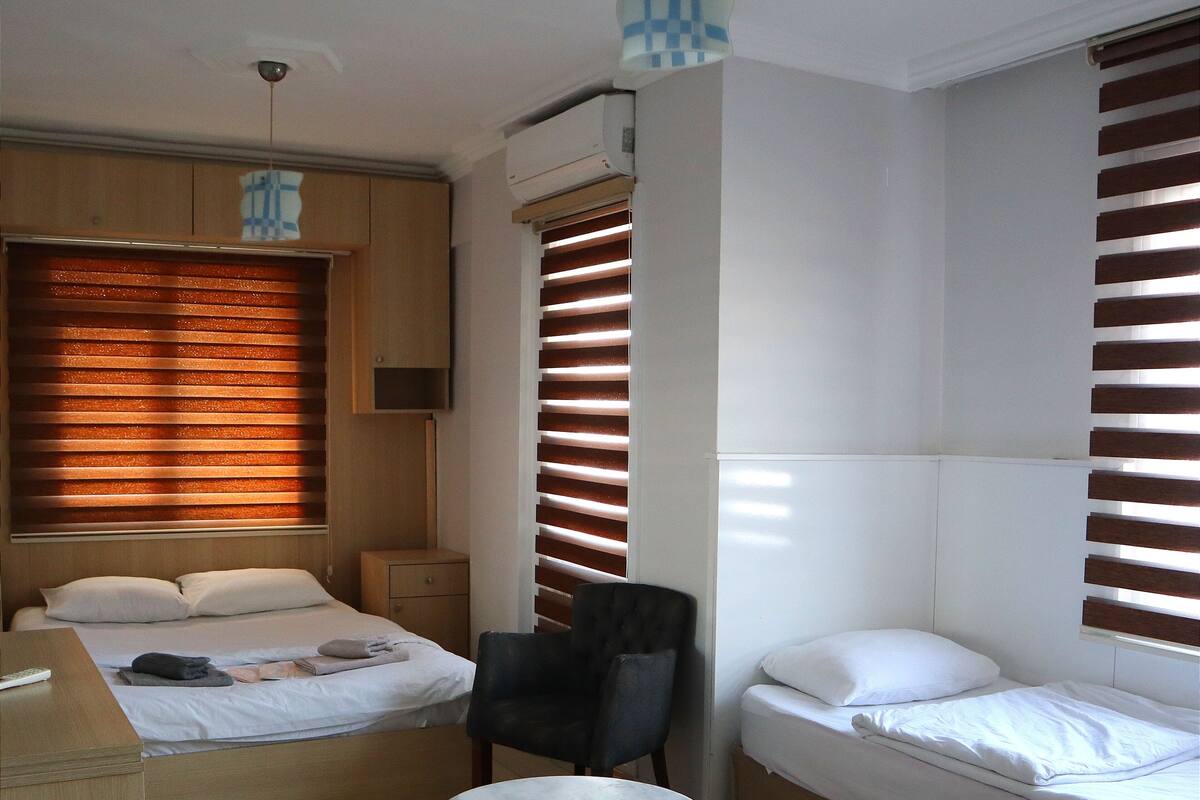 Habitación de hotel compacta con dos camas individuales, una mesita, una silla y una lámpara en el techo.