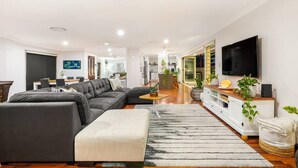 A modern living room with a sectional sofa, a flat-screen TV, and a dining area in the background.
