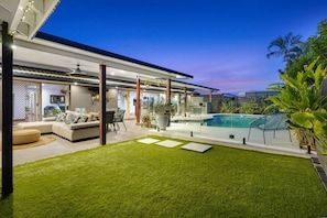 A modern house with a swimming pool, a grassy backyard, and a patio area with outdoor furniture.