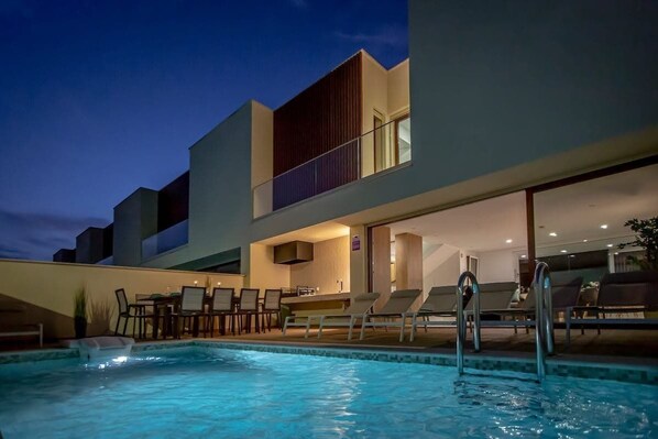 A modern building with a swimming pool, outdoor seating, and a bar area.