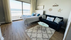 A bedroom with a bed, a nightstand, a dresser, a window with curtains, a ceiling fan, and a view of the ocean. - Ocean view Studio, 10 min walk to pier park, right across from Sharkys (Panama City Beach)
