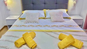 Una cama bien tendida con cabecera gris, dos almohadas blancas y dos toallas amarillas.