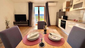 Una sala de estar moderna con un televisor de pantalla plana, una mesa de comedor con platos y una copa de vino, y vistas al exterior a través de amplios ventanales.