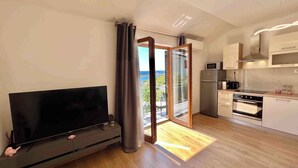 Un apartamento moderno con televisor de pantalla plana, una cocina con microondas y horno, y un ventanal corredero que da a un balcón con vistas.