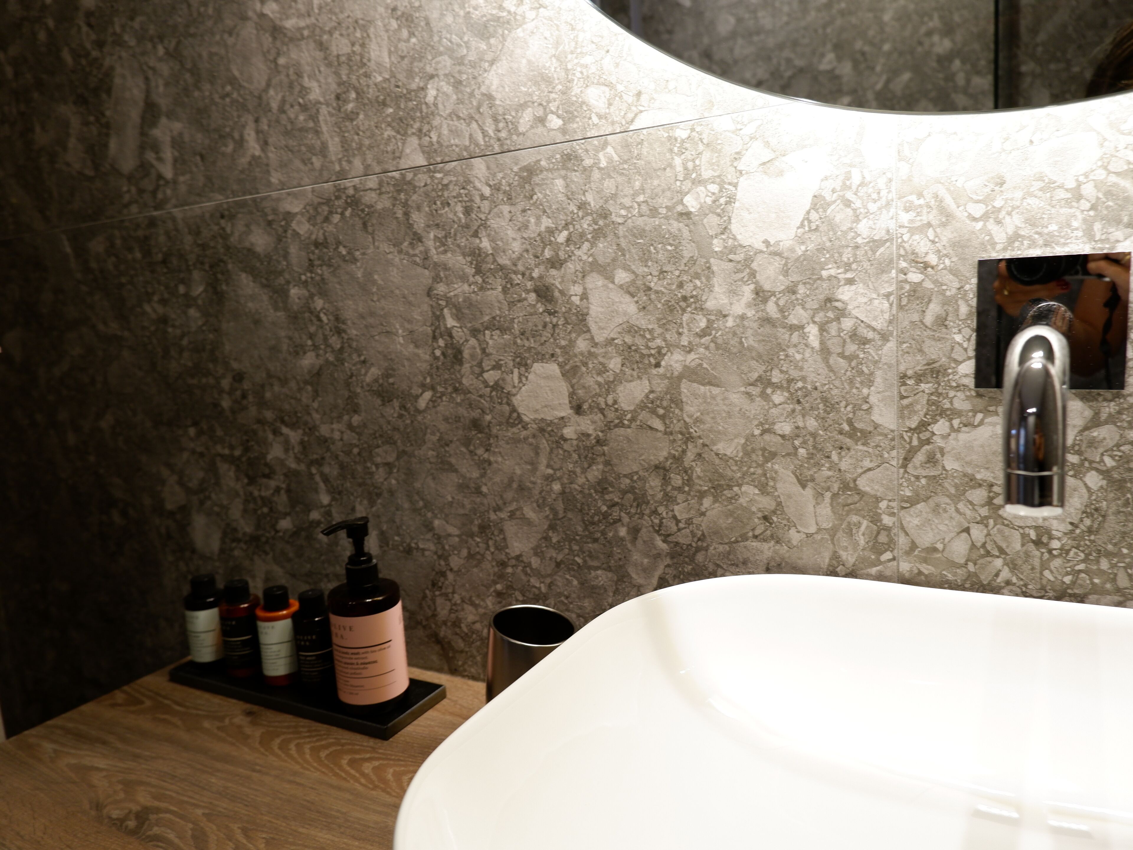 A bathroom with a marble wall, a sink, and a mirror.