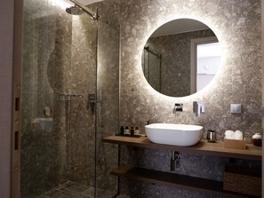 A modern bathroom with a glass-enclosed shower, a round mirror, and a white sink. - Kaiser Luxury Suites (Corfu)