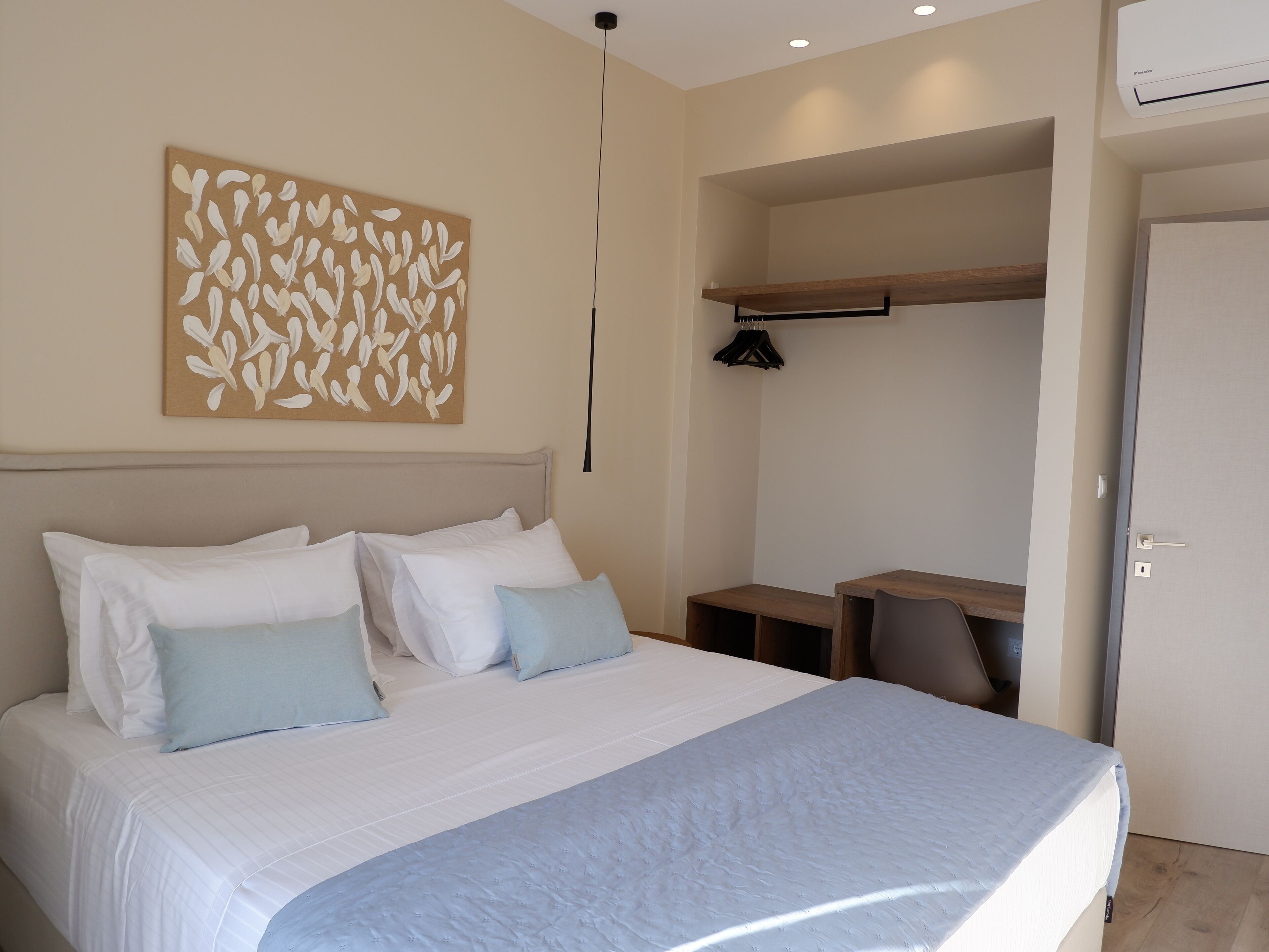 A bedroom with a bed, pillows, a wall art piece, a desk, and a door.