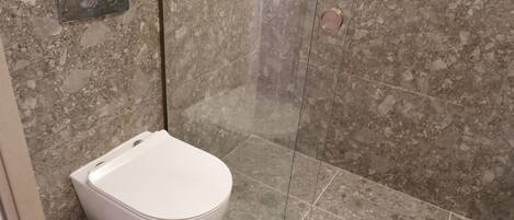 A bathroom with a toilet, a trash bin, and a shower area with a glass door.