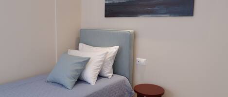 Une chambre à coucher avec un lit, des oreillers, un tabouret rond en bois et un tableau accroché au mur.