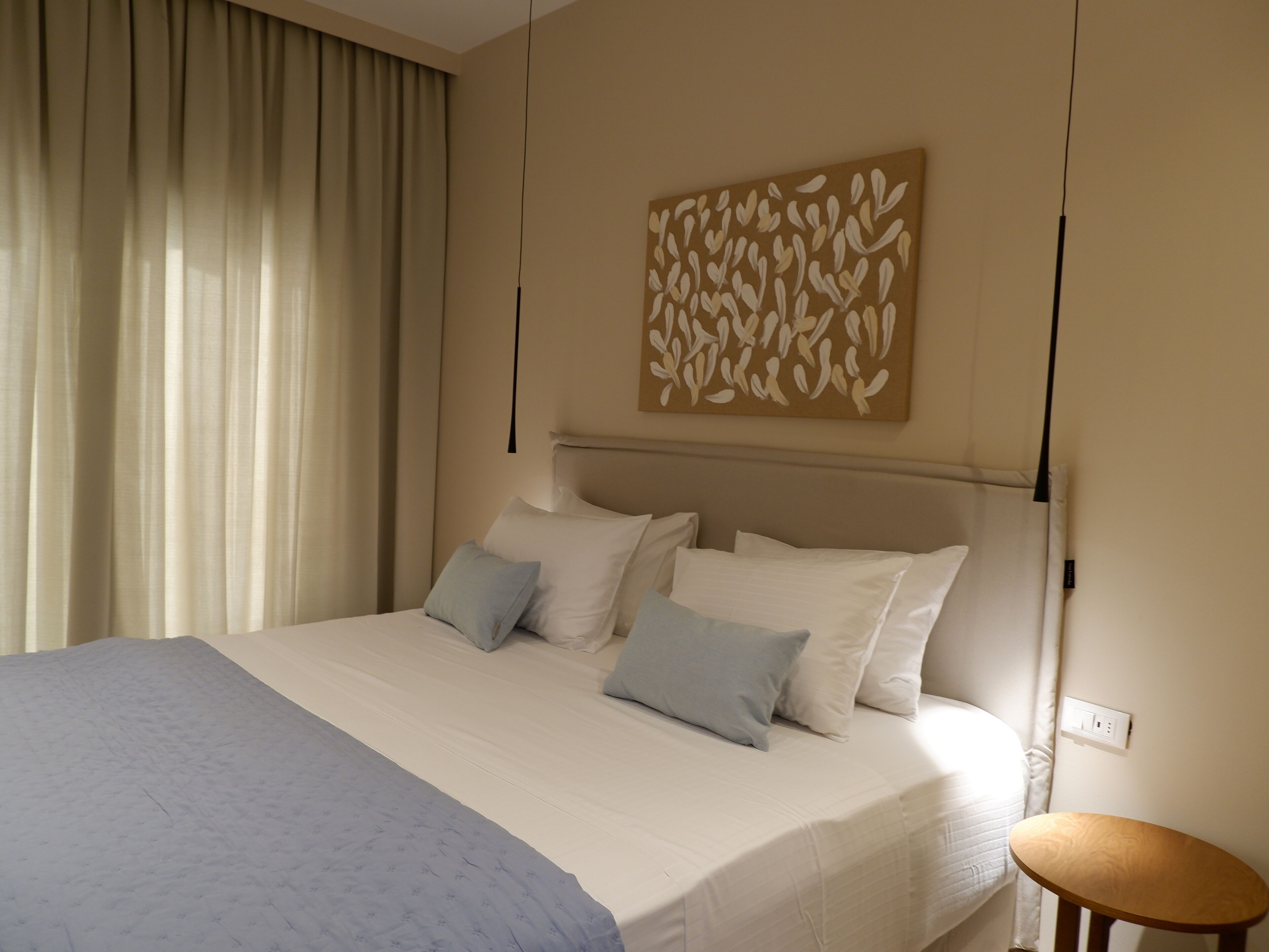 A neatly made bed with white and light blue bedding, a wall-mounted artwork, and a bedside table.
