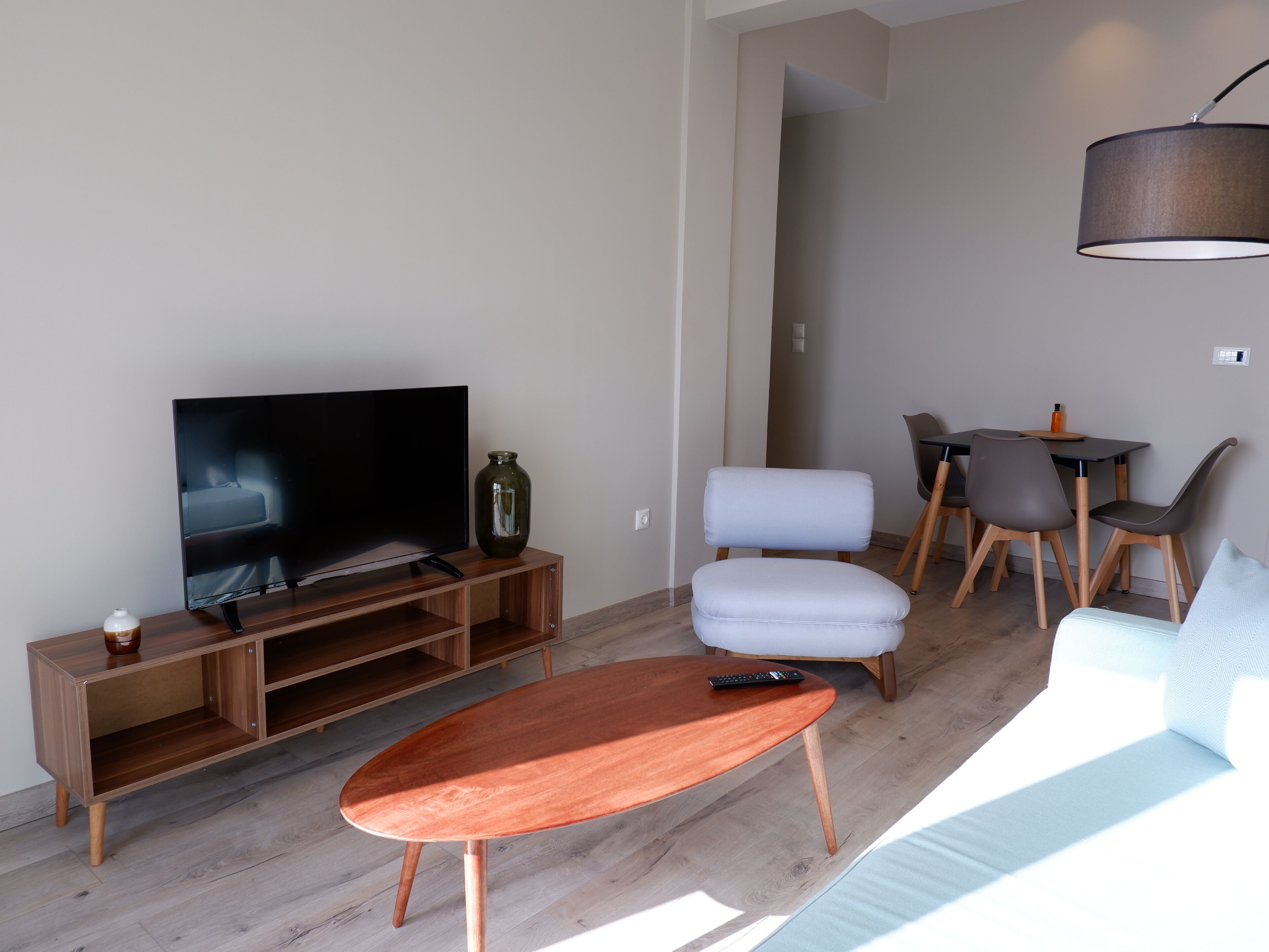 Een moderne woonkamer met een flatscreen televisie op een houten standaard, een salontafel, een bank en een eethoek met stoelen en een tafel.