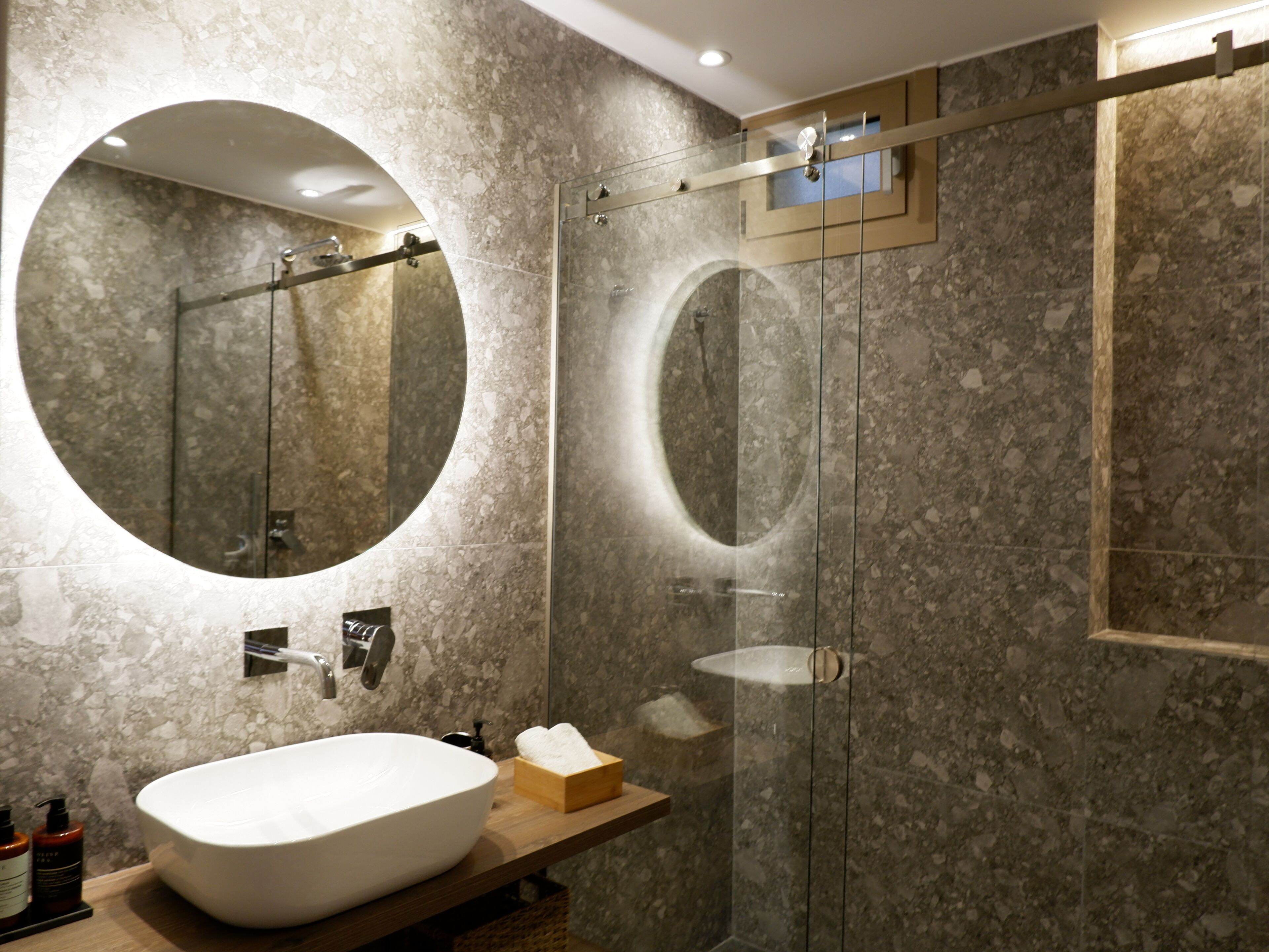 A modern bathroom with a large oval sink, a round mirror, and a glass-enclosed shower.