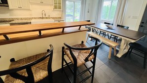 A modern kitchen with white cabinets, a wooden island, and a dining area with a bench and chairs. - This House Got RIZZ - Recently Renovated Lake Thompson Canal Home (Howell)