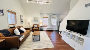 A modern living room with a brown leather sofa, a wooden coffee table, and a flat-screen TV on a white cabinet. - This House Got RIZZ - Recently Renovated Lake Thompson Canal Home (Howell)