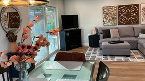 Una sala de estar moderna con una mesa de comedor de vidrio, un sofá, un televisor y decoración en la pared.