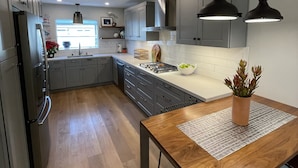 Una cocina moderna con armarios grises, una mesa de comedor de madera y luces colgantes.