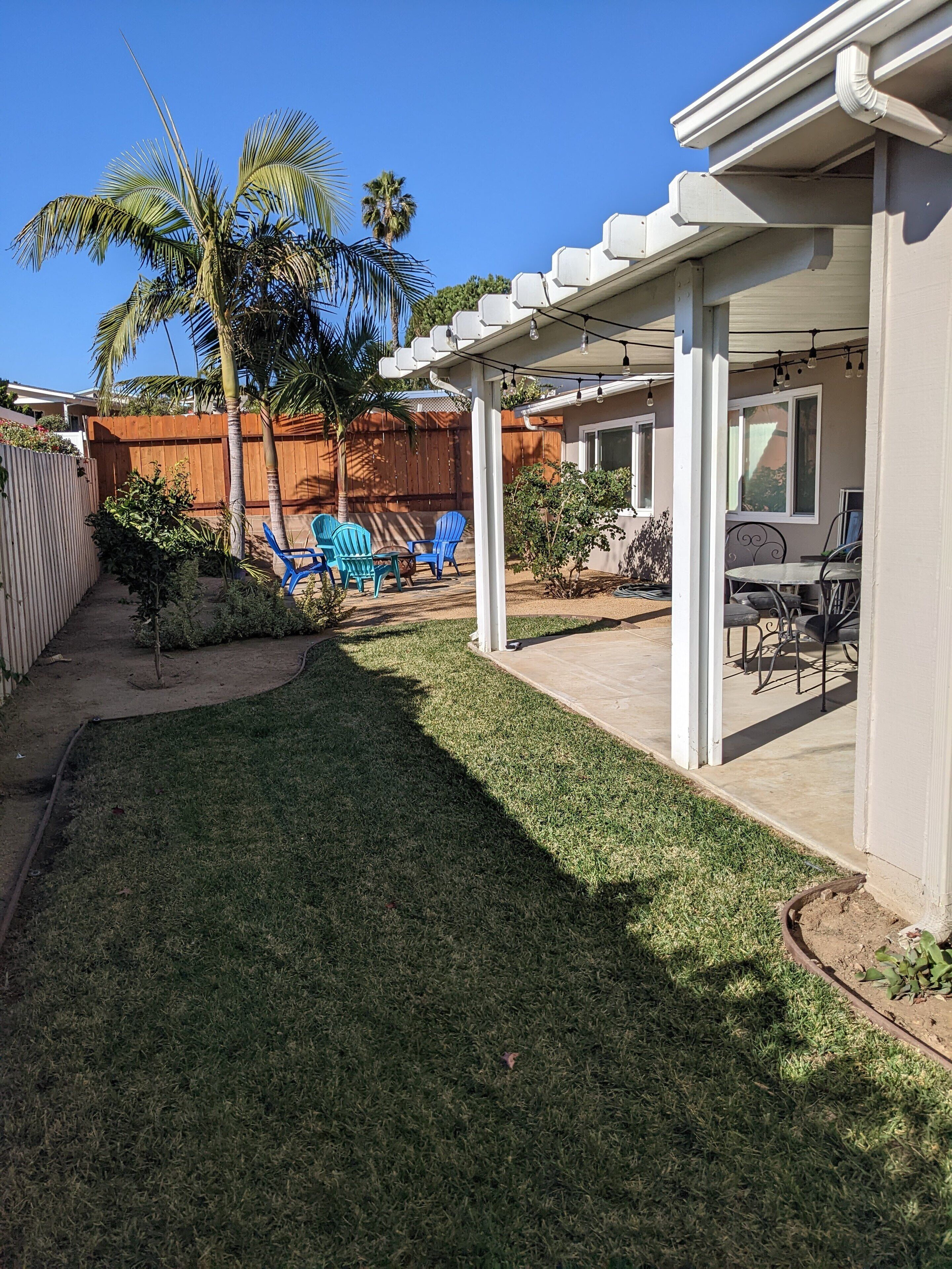 A covered patio area with a lawn, outdoor seating, and a wooden fence.