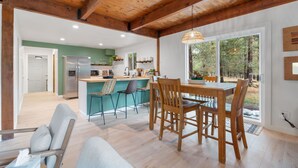Una cocina amplia con techo de madera, un comedor con sillas de madera y vistas al exterior a través de grandes ventanales.