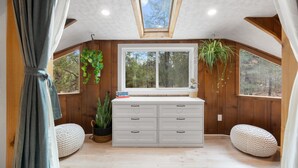Un dormitorio acogedor en el ático con tragaluces, paredes de madera, un ventanal grande y dos sillones de ante blancos.