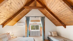 Un dormitorio con techo inclinado, una cama, un aparador y un ventanal con cortinas.