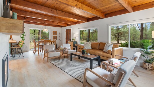 Un espacio habitable amplio con un techo de madera alto, ventanas grandes que ofrecen vistas al exterior, un rincón de estar acogedor y un comedor.