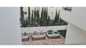 A courtyard with white walls, a tiled floor, and several rectangular planters with small plants. - APPART CENTRAL LAC 2 T.H.STANDING (Les berges du lac)