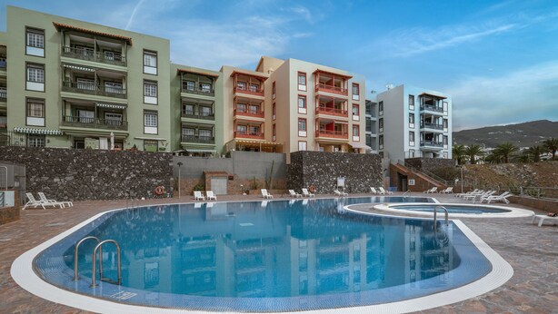 Piscina com deck de pedra, rodeada por cadeiras de descanso e um muro de pedra.