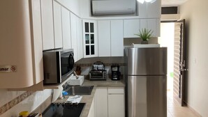 Una cocina compacta con armarios blancos, un refrigerador de acero inoxidable, un microondas, una cafetera y un ventilador de techo.